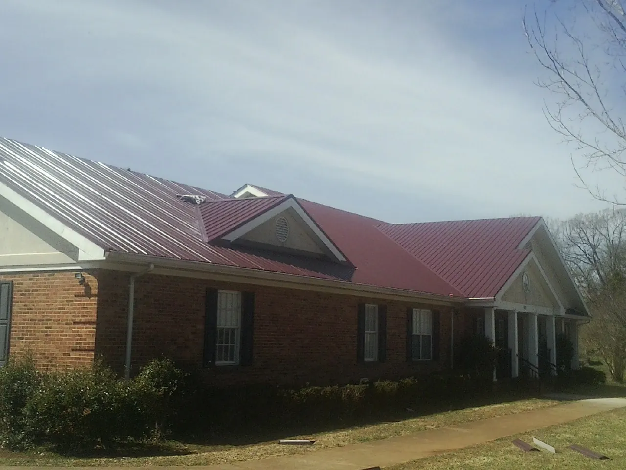 Red metal roof with gabled entries on a long brick building, from a Hail Damage Roof Repair job in Poplarville
