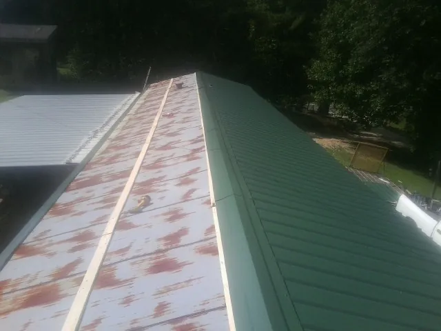 Old rusted panels beside newly installed green metal roofing — Wind Damage Roof Repair by Roofing Brothers in Poplarville