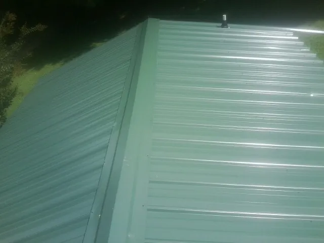 New green metal panels meeting at the ridge of a roof — Flat Roof Repair work by our crew in Poplarville