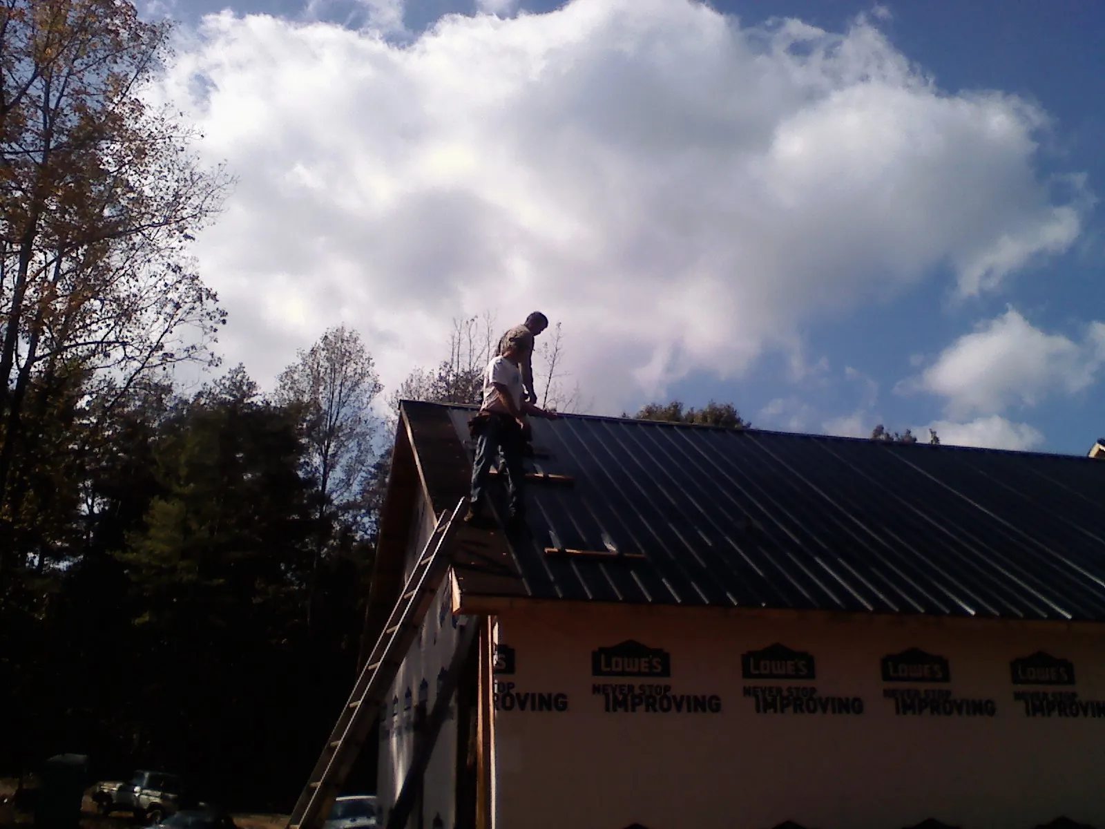 Roofer fastening dark metal panels high against a cloudy sky, from a Roof Inspection job in Poplarville