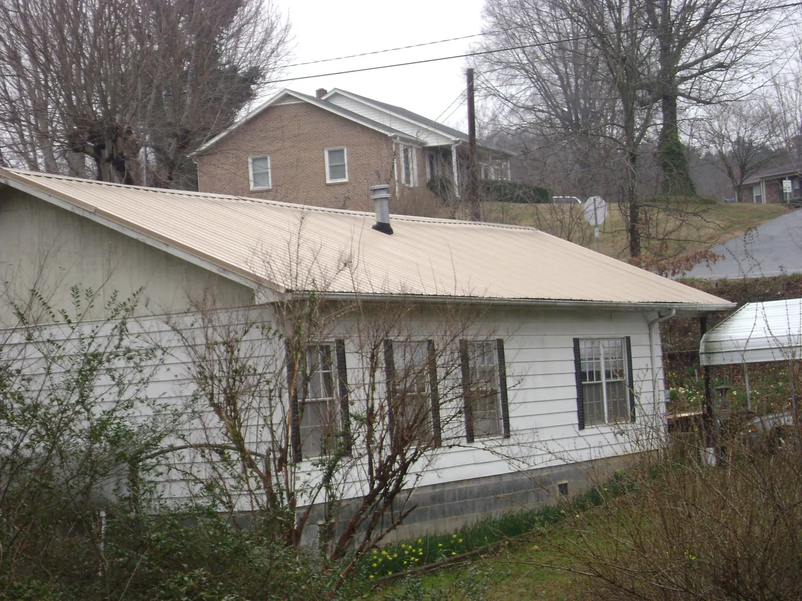 Tan metal roof on a white sided house set into a hillside — Commercial Roofing by Roofing Brothers in Poplarville