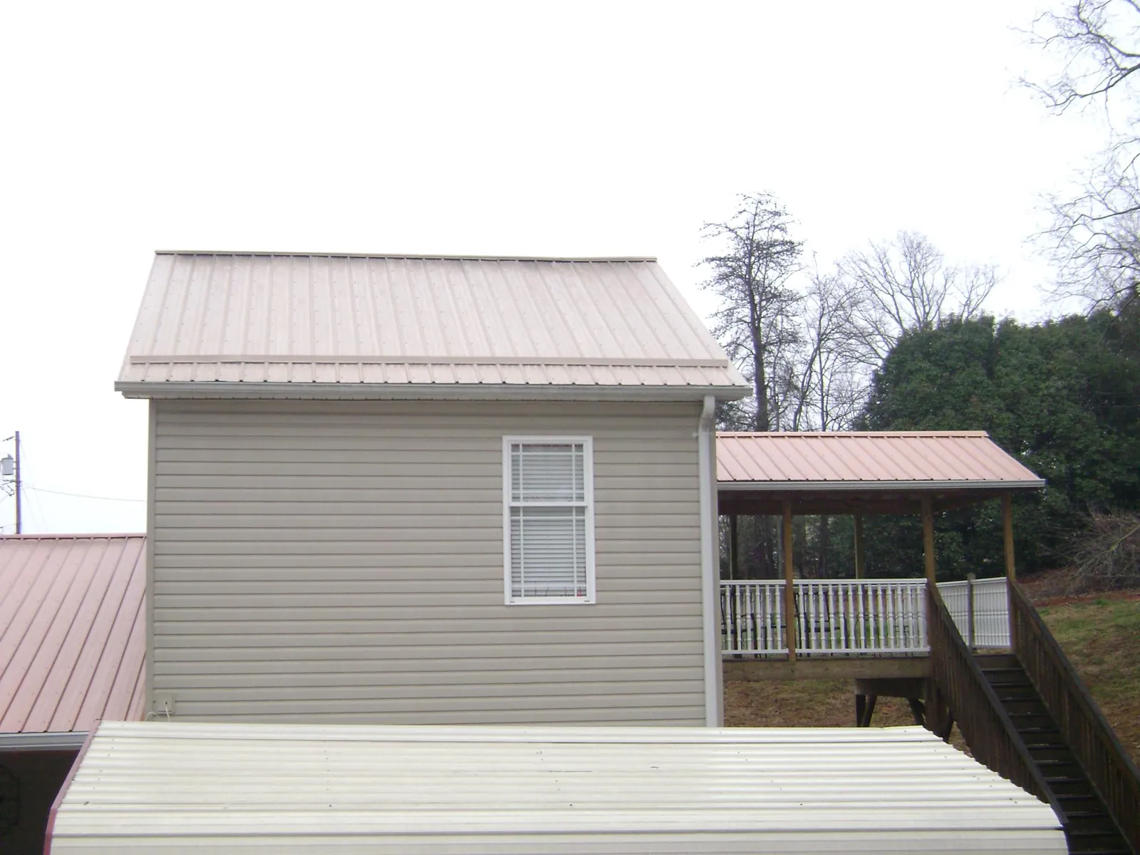 Tan metal roofs on a two story addition and attached porch, from a Roof Replacement job in Poplarville